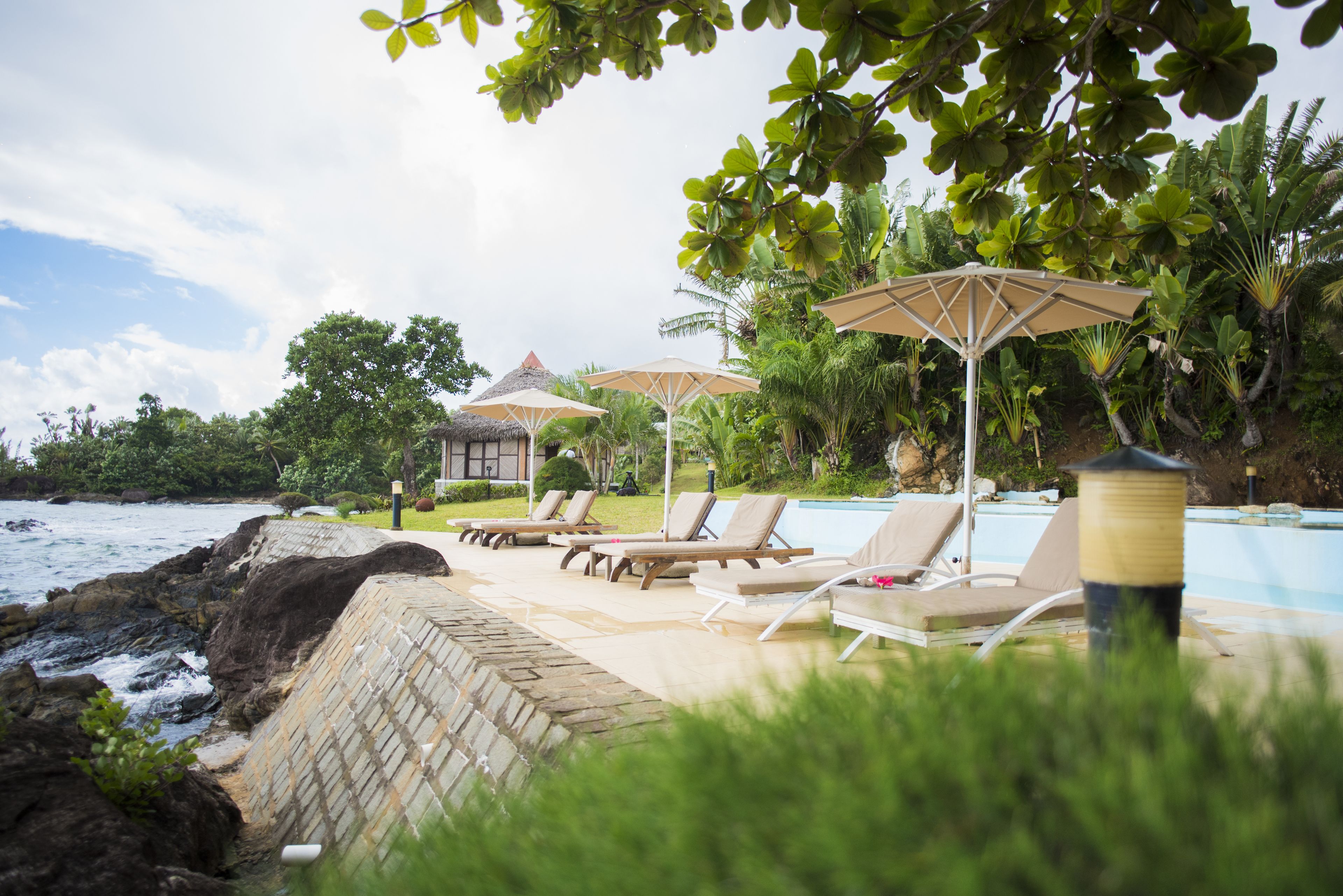 Un área junto a la piscina con sillones y sombrillas, una estructura de techo de paja y vista al océano.