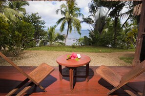 A wooden deck with a round table and two chairs, overlooking a beach with palm trees and the ocean. - Masoandro Lodge (Nosy Boraha)