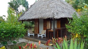 A thatched-roof hut with two white chairs and a table, surrounded by tropical plants and a gravel path. - Masoandro Lodge (Nosy Boraha)