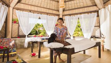 Relax in a serene spa setting with a massage table, surrounded by lush greenery views and a thatched roof ceiling.