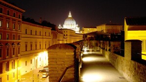 A nighttime view of a historic cityscape with a prominent dome-lit building in the background, a stone bridge, and a canal. - Al Passetto St. Peter's bike (Rome)