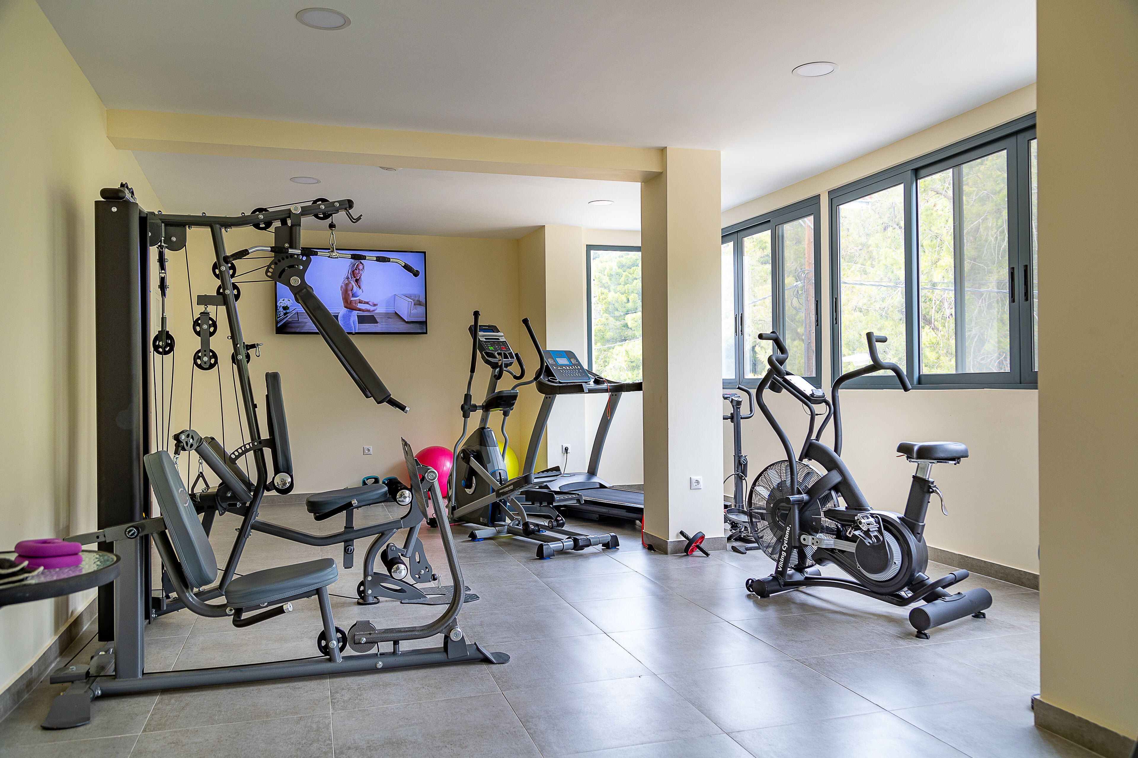 Een sportschool thuis met diverse fitnessapparaten, waaronder een loopband, een hometrainer en krachtapparaten.