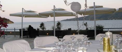 An outdoor dining area with tables set for a meal, overlooking a body of water.