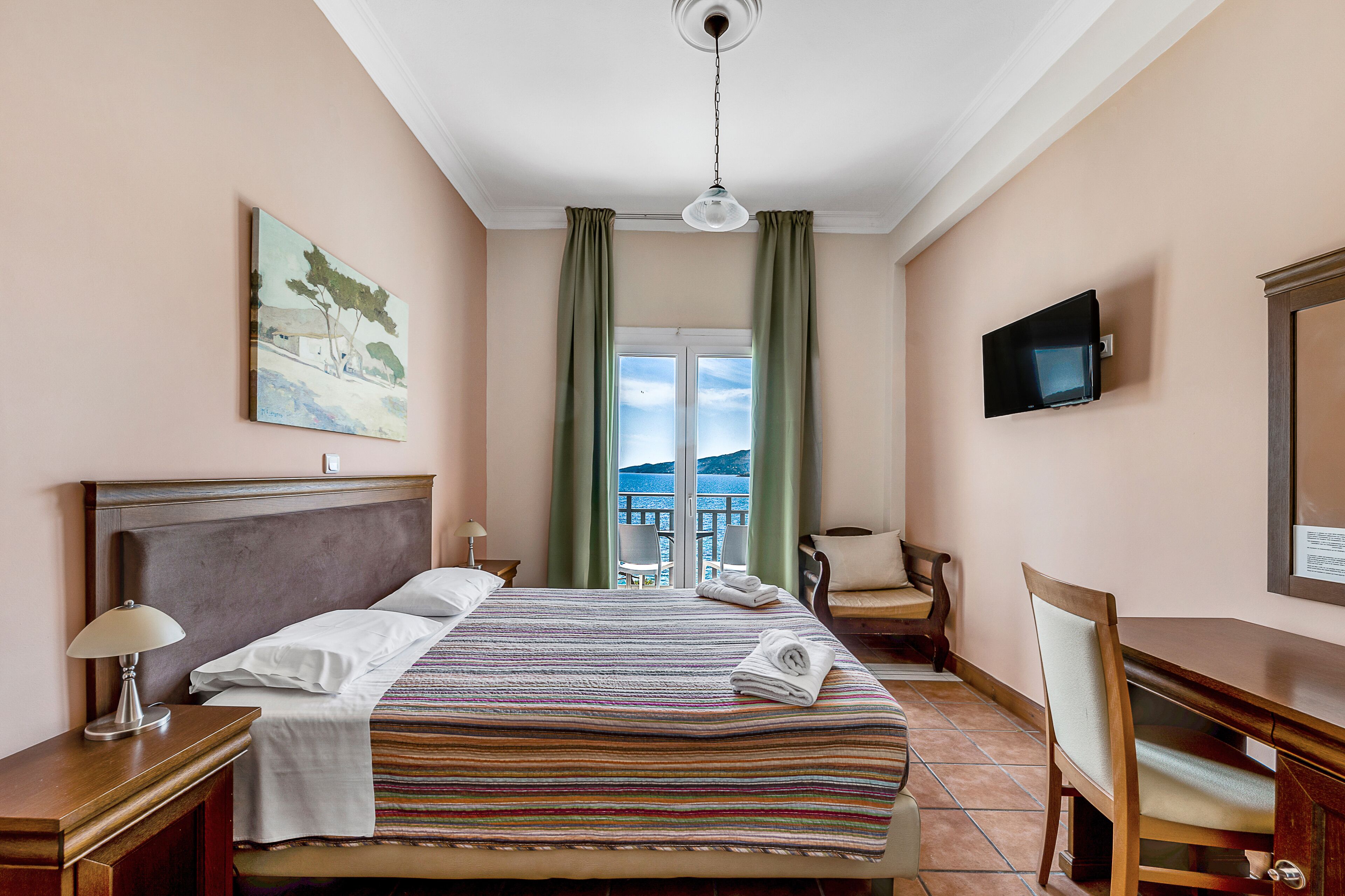 A hotel room with a bed, a desk, a chair, a TV, and a painting on the wall.