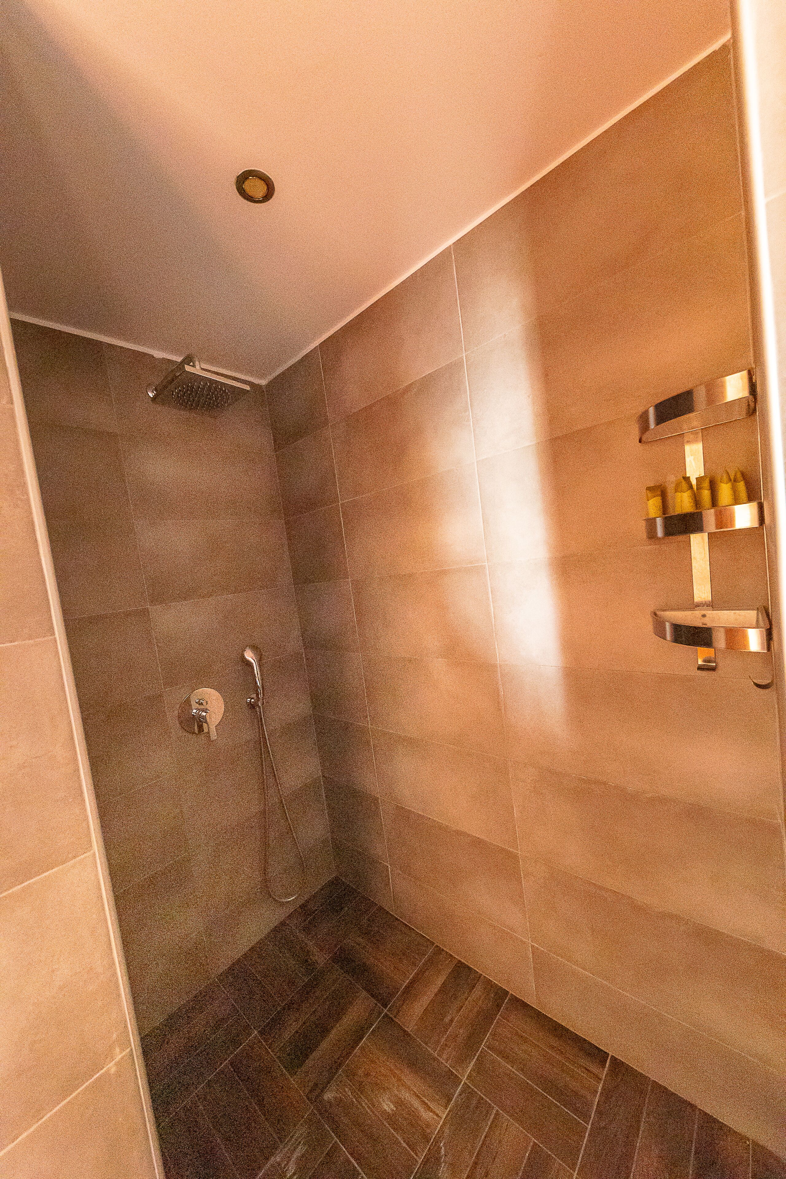 Una ducha a ras de suelo con paredes de azulejos y suelo de madera.