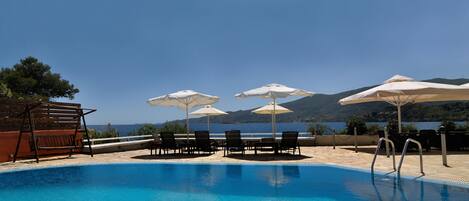 A swimming pool with lounge chairs and umbrellas, overlooking a body of water and hills.