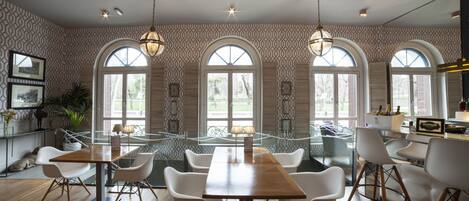 Un comedor con una larga mesa de madera, sillas blancas y ventanas de arco.