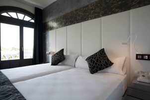 Habitación de hotel con dos camas, un ventanal grande, un teléfono y una lámpara fijada a la pared.