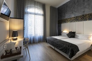 A modern hotel room with a large bed, a desk with a lamp, and a chair.