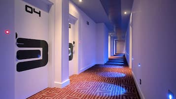 En modern hotellkorridor med ett mönstrat golv, vita väggar och upplysta siffror på väggarna.