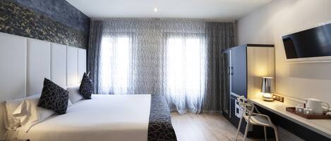 Habitación de hotel con una cama grande, un escritorio con silla, televisor y ventana con cortinas.
