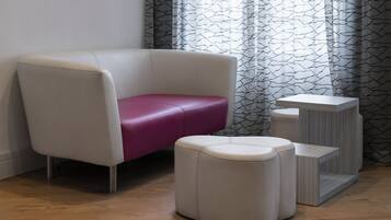 Una habitación moderna con un sillón blanco, un reposapiés rosa y una mesita auxiliar blanca.