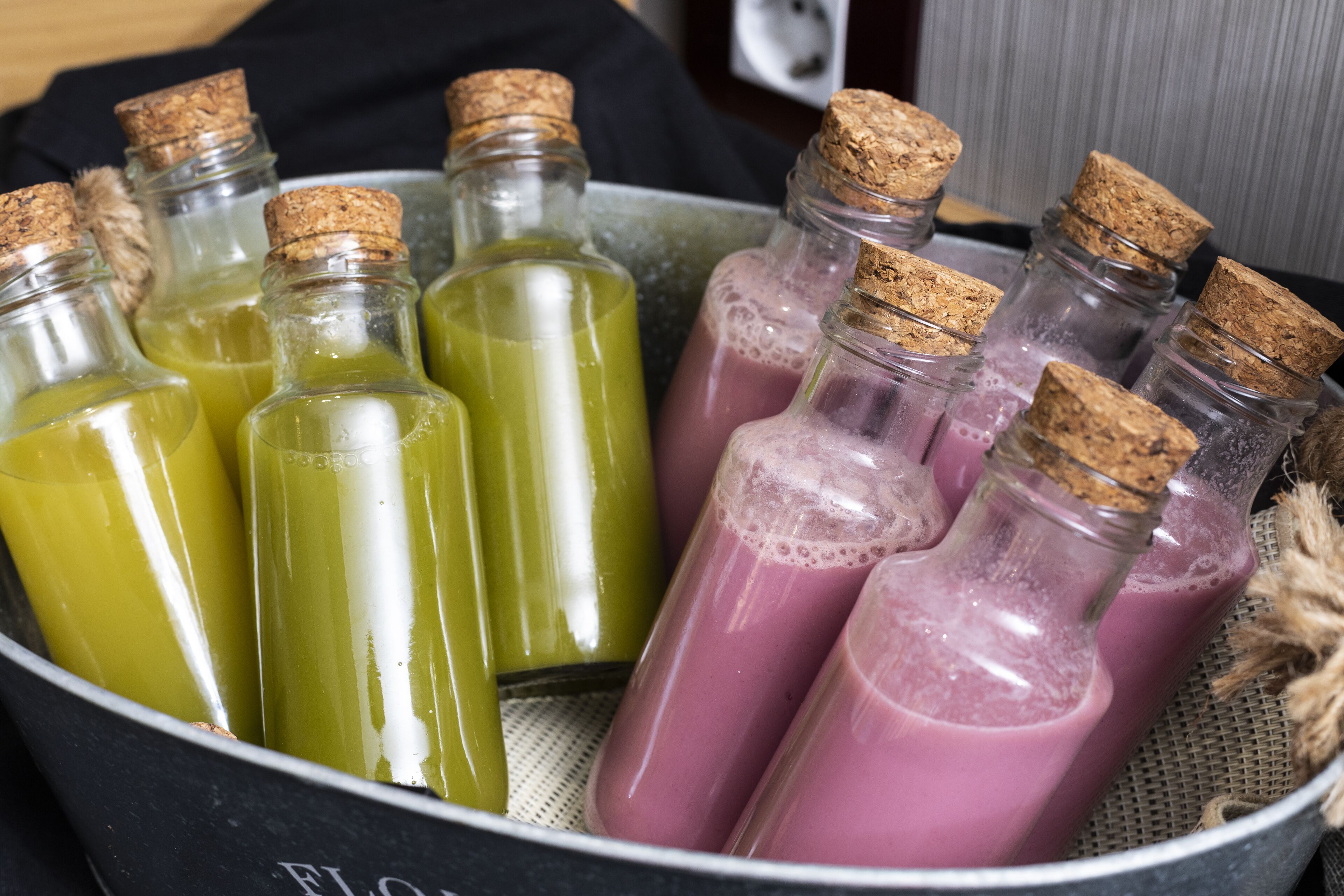 Un recipiente con varias botellas de vidrio con tapones de corcho, llenas de líquidos de diferentes colores.