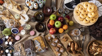 A table with various food items, including fruits, pastries, and jars of preserves.