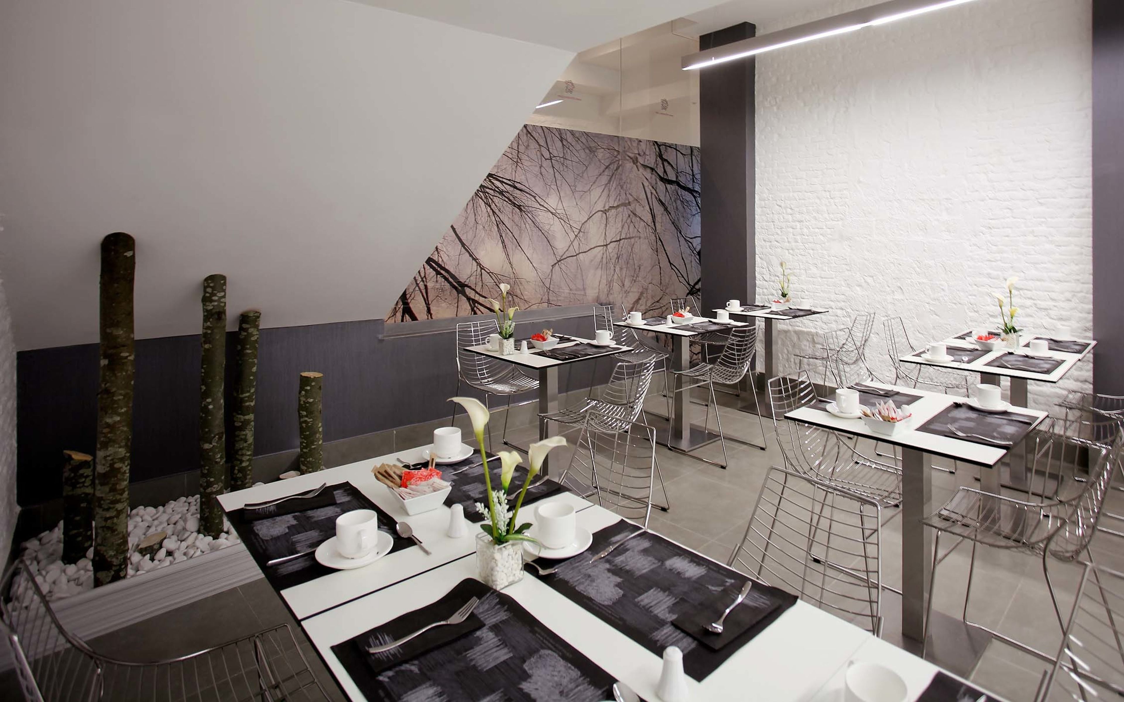Un restaurante moderno con diseño minimalista, destacando mantelería blanco y negro, sillas de vidrio transparente y una pared de mármol con un diseño de hojas.