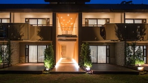 A modern two-story house with a central entrance, a balcony on the upper floor, and a well-lit pathway leading to the entrance. - Doi Tung Lodge (Mae Fa Luang)