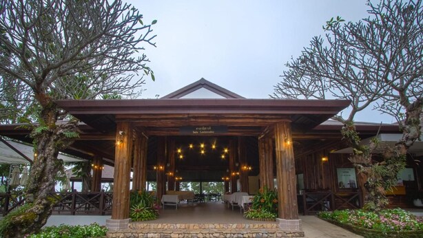 A covered outdoor seating area with tables and chairs, surrounded by trees and plants. - Doi Tung Lodge (Mae Fa Luang)