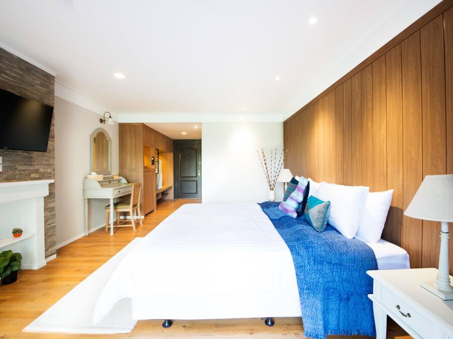Ein modernes Schlafzimmer mit einem großen Bett, einem an einer Holzwand montierten Fernseher, einem Schreibtisch und einem Stuhl.
