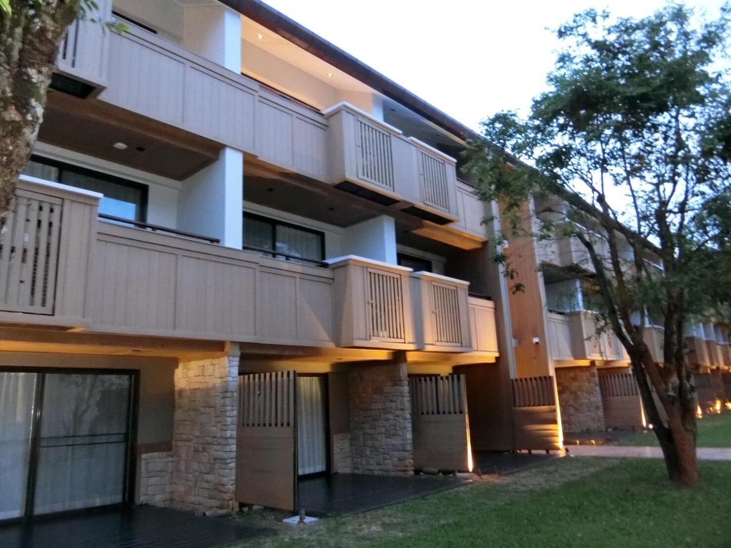 A multi-story hotel with balconies, stone pillars, and a well-maintained lawn.