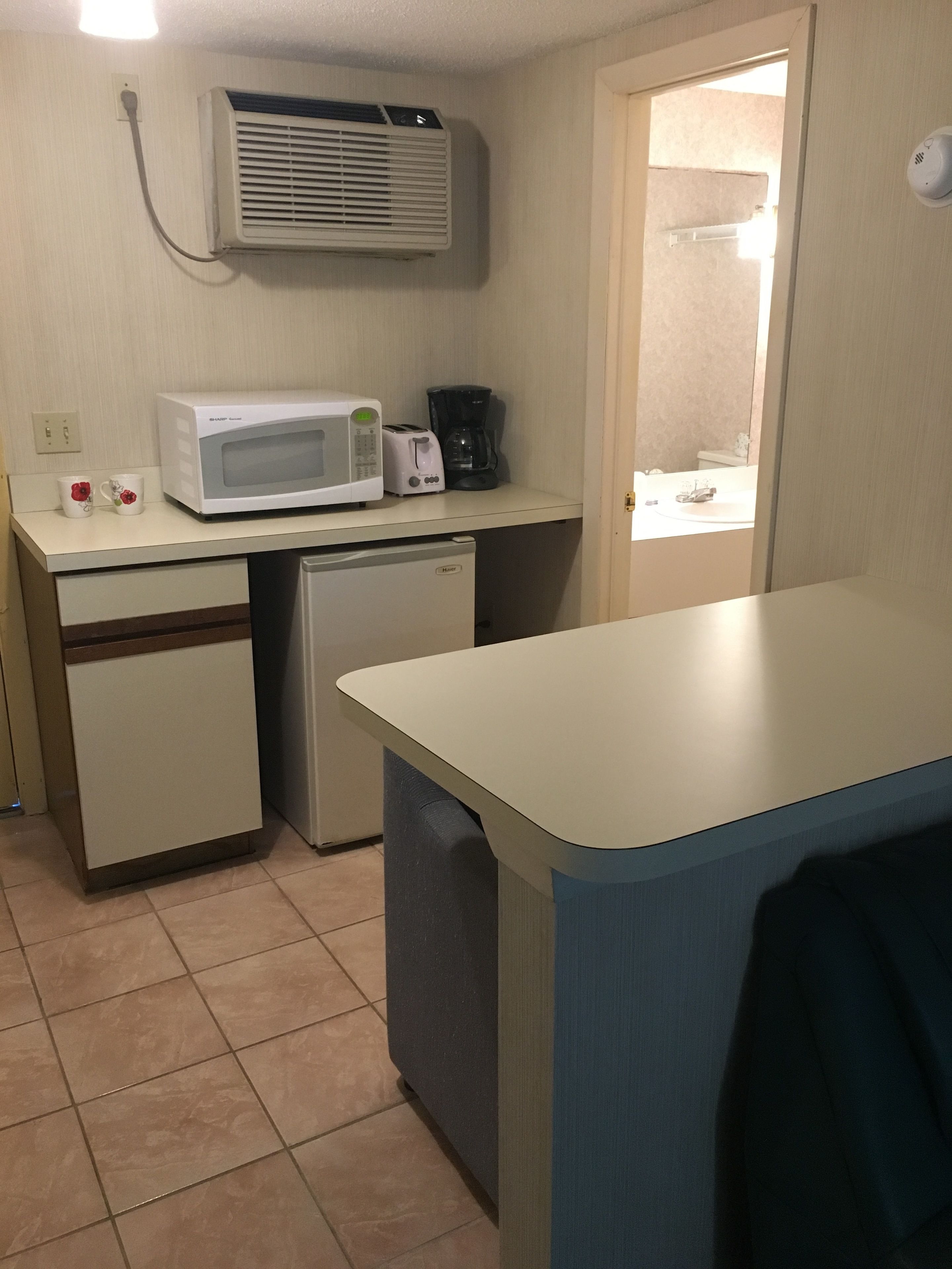 A compact kitchenette with a microwave, toaster, and coffee maker on a counter, a small refrigerator, and a dishwasher.