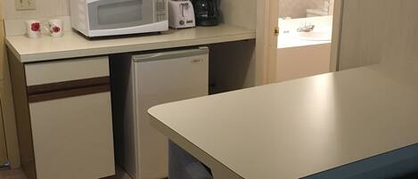 A compact kitchenette with a microwave, toaster, and coffee maker on a counter, a small refrigerator, and a dishwasher.