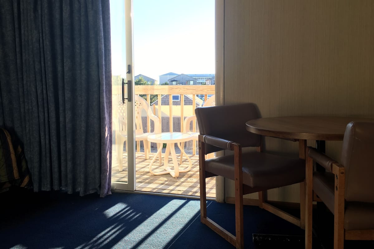 A room with a wooden table and two chairs, a sliding glass door leading to an outdoor area with a wooden deck and a view of buildings.
