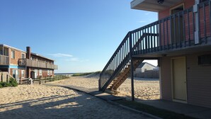 A beachside building with a wooden staircase leading to a balcony, adjacent to a sandy beach. - Beachfront White Sands (North Truro)