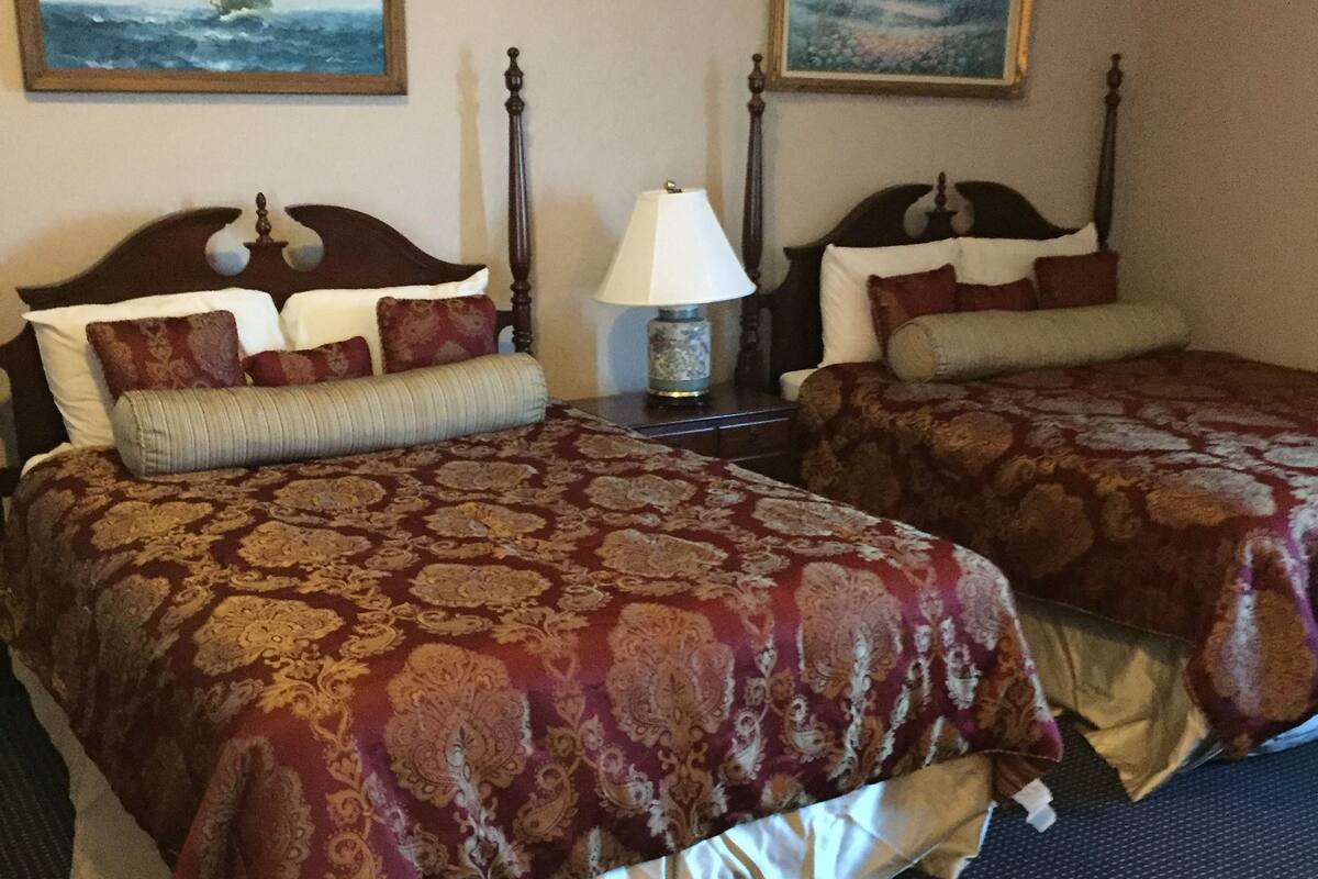 A hotel room with two beds, each with a patterned bedspread, a nightstand with a lamp, and two framed paintings on the walls.