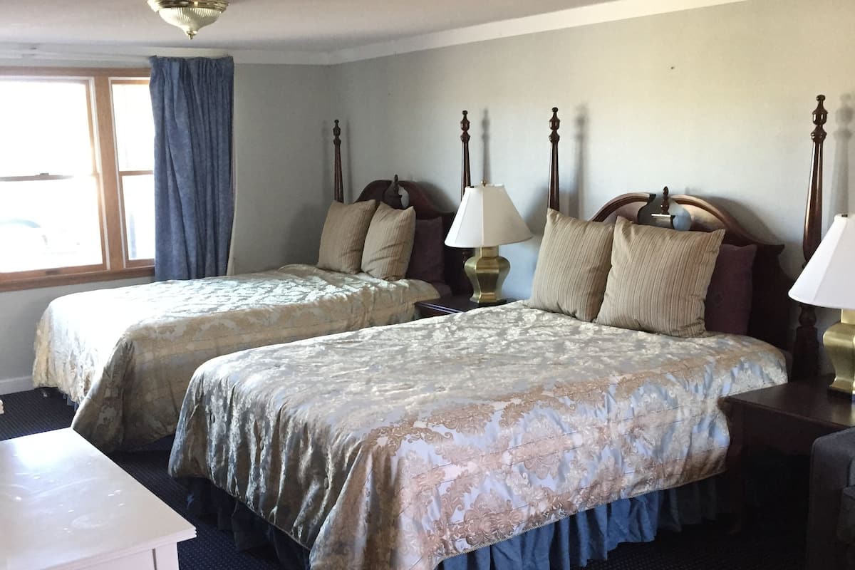 A hotel room with two beds, a small table, and a window with curtains.