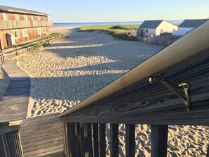 Vista de la playa desde una terraza de madera, con una playa arenosa, una valla de madera y un edificio al fondo.