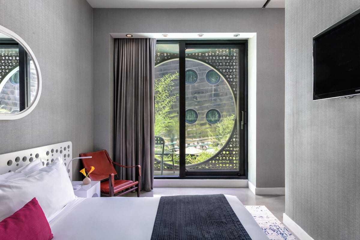 A modern hotel room with a large bed, a TV mounted on the wall, and a view through a circular window.