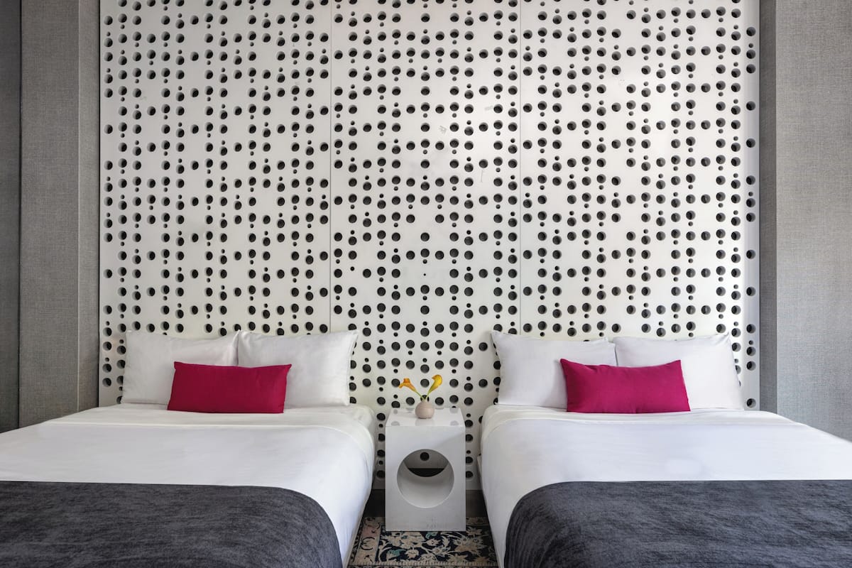 A hotel room with two beds, a polka dot headboard, and a small bedside table with a vase of flowers.