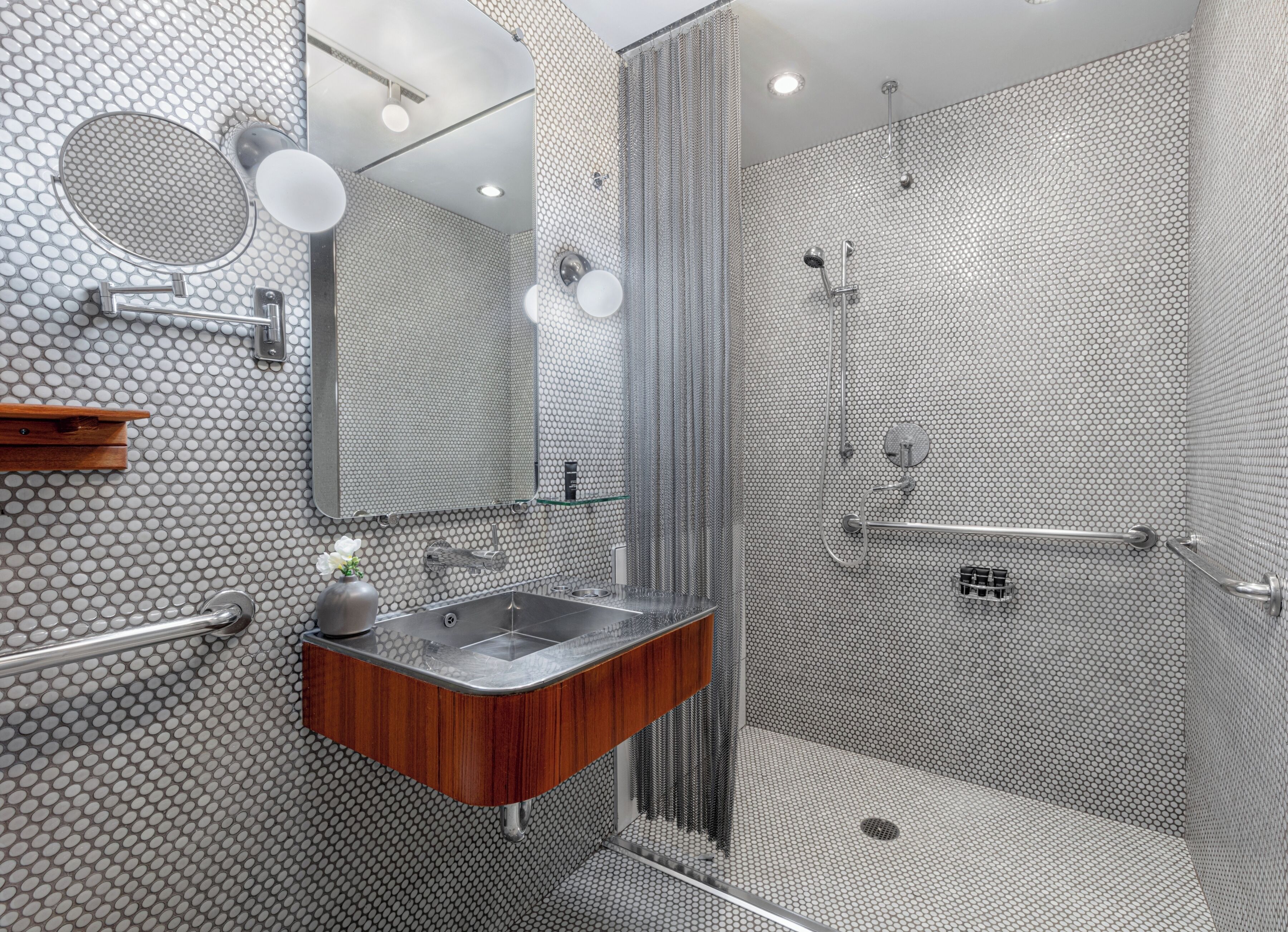 A modern bathroom with a hexagonal patterned tile wall, a wooden vanity with a sink, a mirror, and a shower area with a glass door.