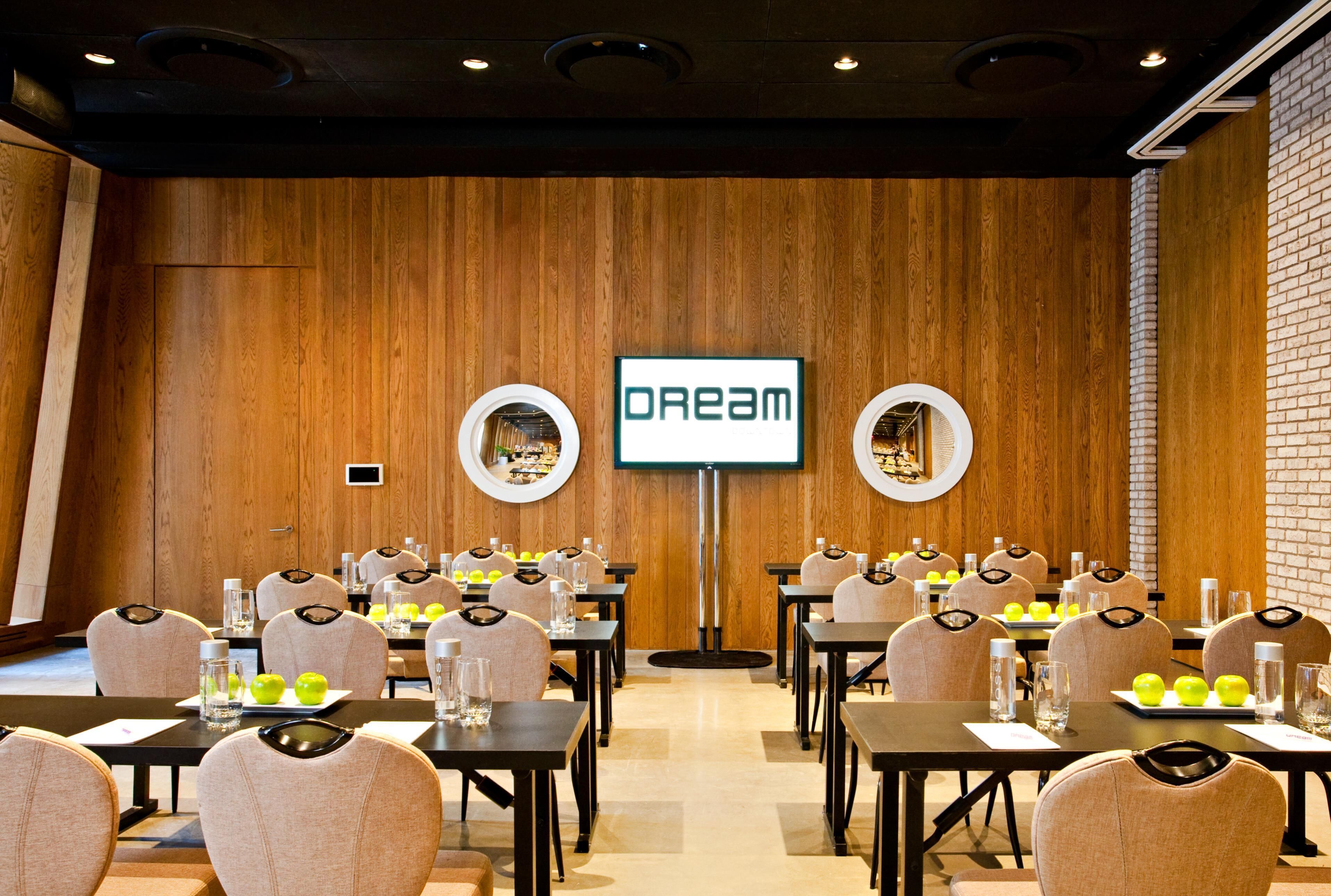Una sala de conferències amb parets de fusta, una pantalla gran que mostra 'DREAM' i diverses taules amb cadires i ampolles d'aigua.