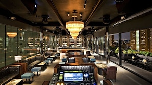 A modern bar with leather seating, a DJ booth, and a large chandelier.