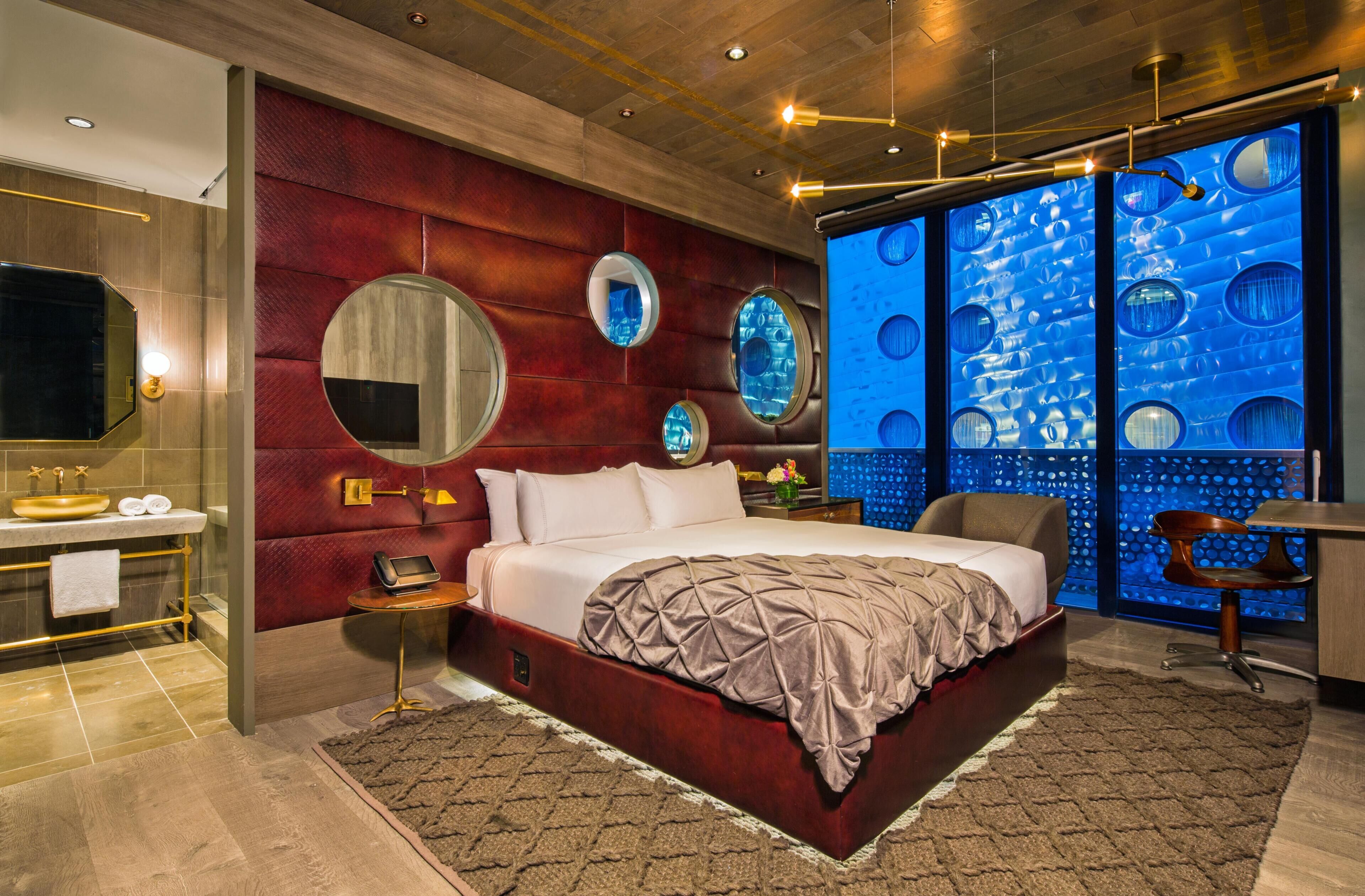 A modern bedroom with a large bed, a vanity with a gold sink, and a unique blue wall feature.
