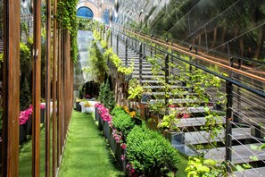A modern atrium with a glass ceiling, green artificial grass, and a variety of plants and flowers. - Dream Downtown, by Hyatt (New York)