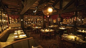 Un restaurant avec des tables rondes, des banquettes et un plafond haut avec des poutres apparentes.