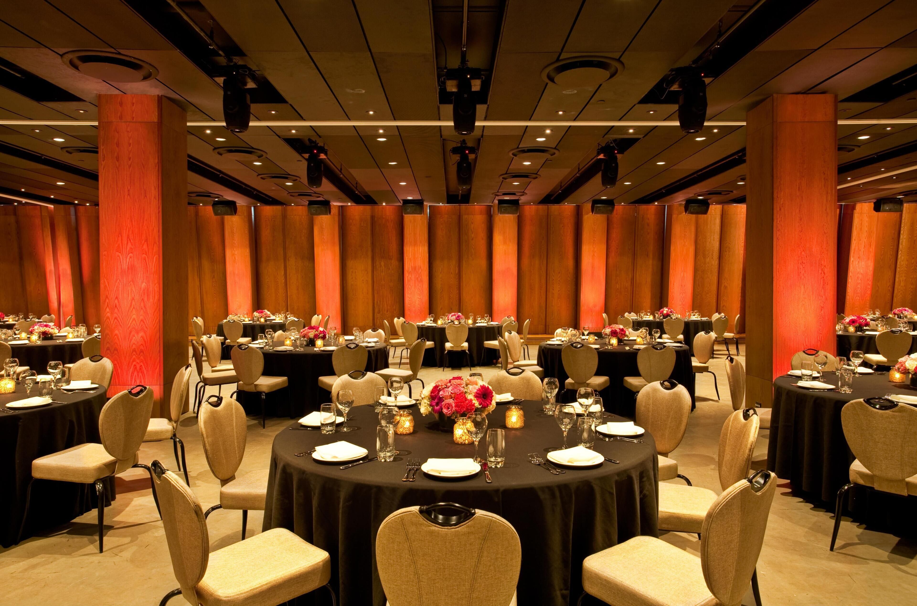Un salón de banquetes con mesas redondas, sillas y centros de mesa florales.
