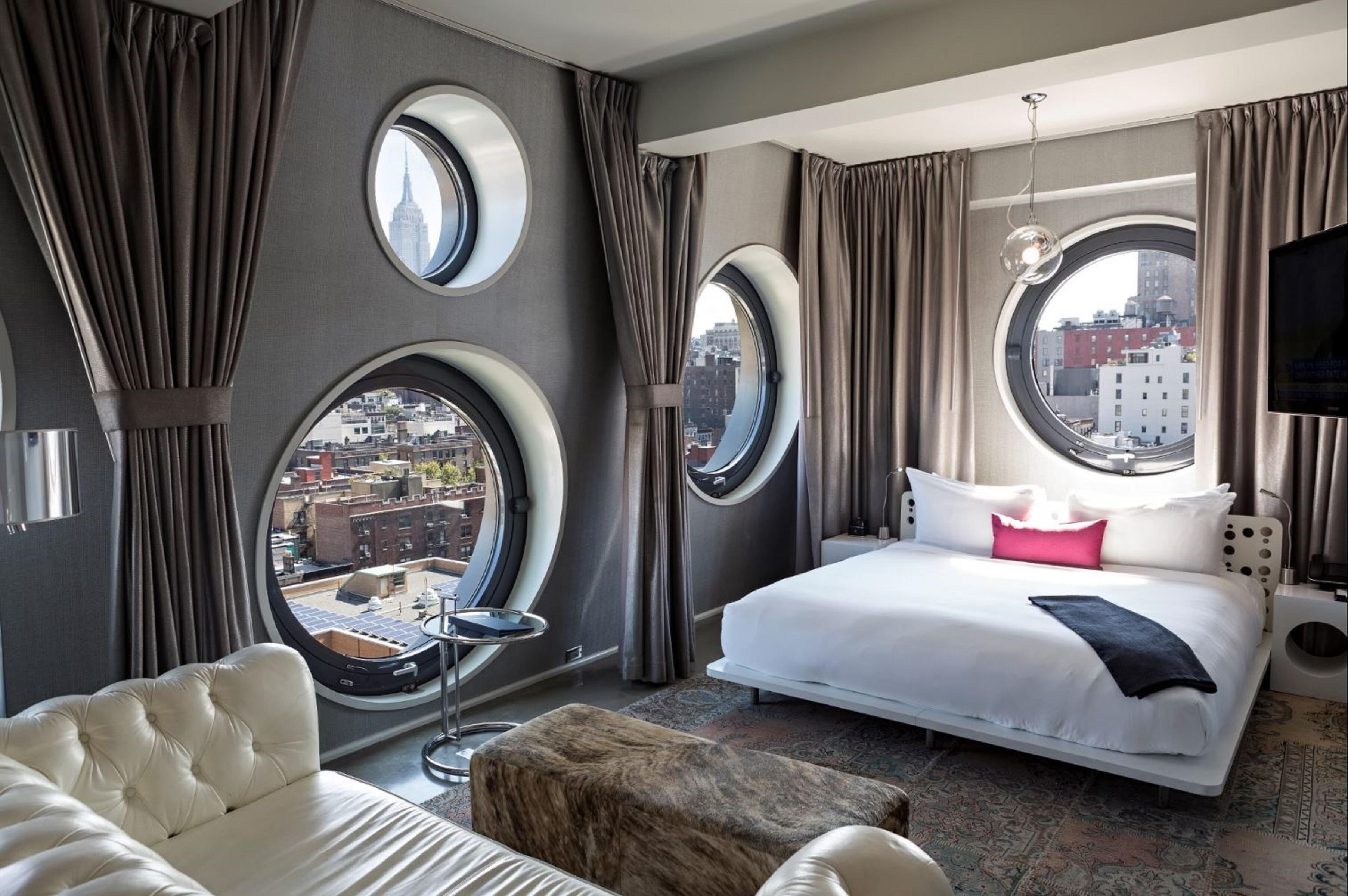 A hotel room with a large bed, a round window, a sofa, and a small table.