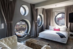 A hotel room with a large bed, a round window, a sofa, and a small table. - Dream Downtown, by Hyatt (New York)