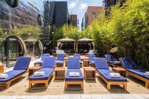 A rooftop lounge area with sun loungers, a covered seating area, and a large mural on the building wall. - Dream Downtown, by Hyatt (New York)