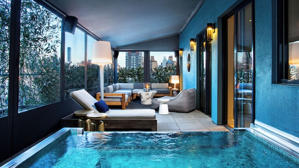A rooftop infinity pool with a seating area, large windows, and city views.