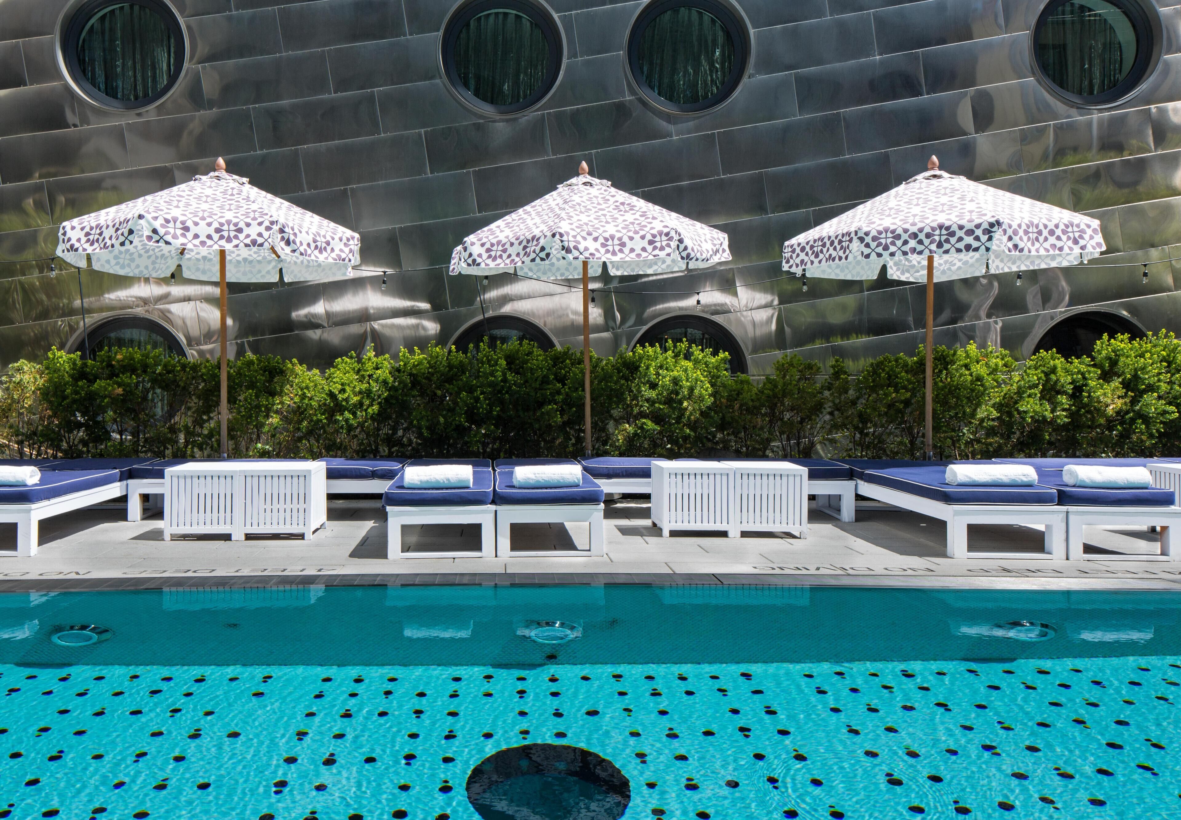 Ein Pool mit Liegestühlen und Sonnenschirmen, umgeben von einem modernen Gebäude mit Rundfenstern.
