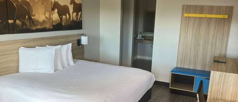 A hotel room with a large bed, a wooden headboard, a painting of horses, a small desk, and a mirror.
