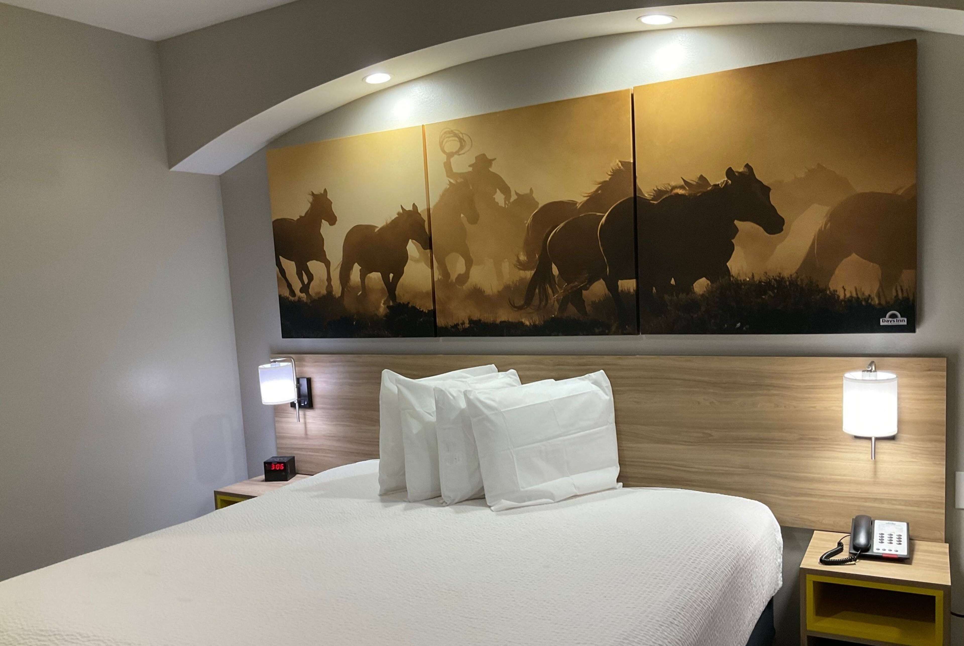Habitación de hotel con un amplio mural en la pared de caballos, una cama bien hecha con almohadas, lámparas de noche y un teléfono en la mesita.