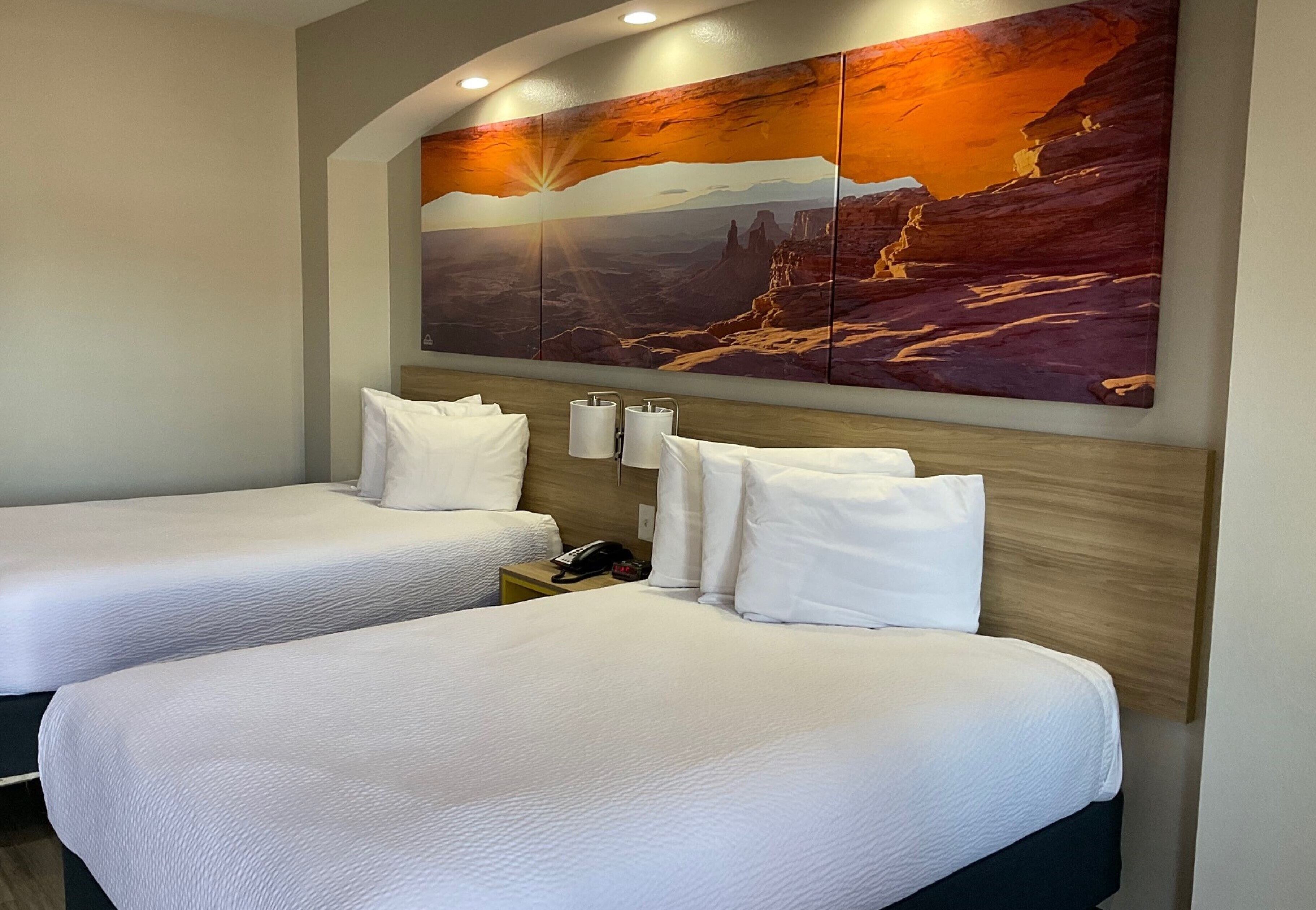 Habitación de hotel con dos camas, un cuadro grande en la pared de un atardecer y cabecera de madera.