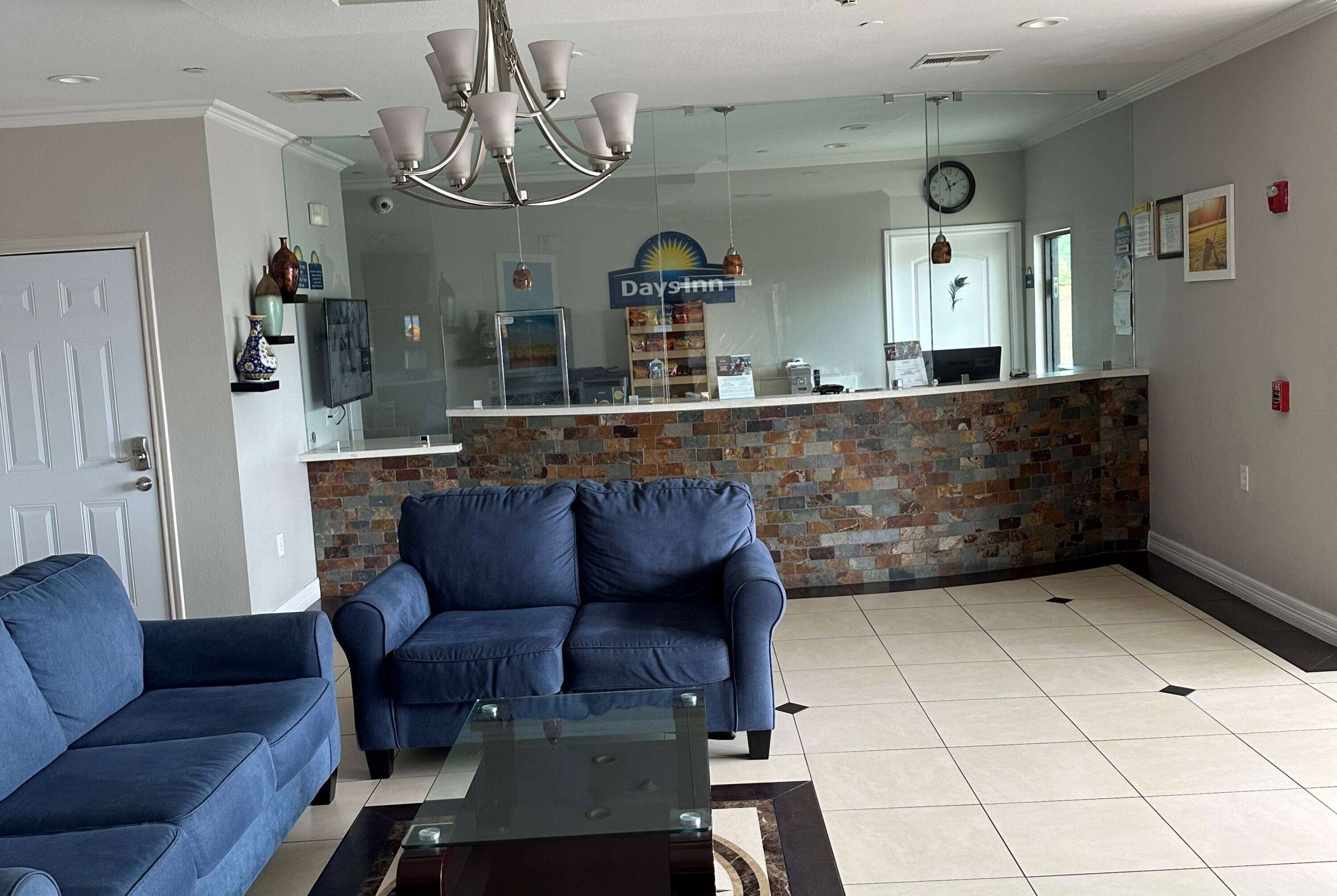 Eine Hotlellobby mit einer Rezeption, einem blauen Sofa, einem Glastisch und einer Kristallleuchtre.
