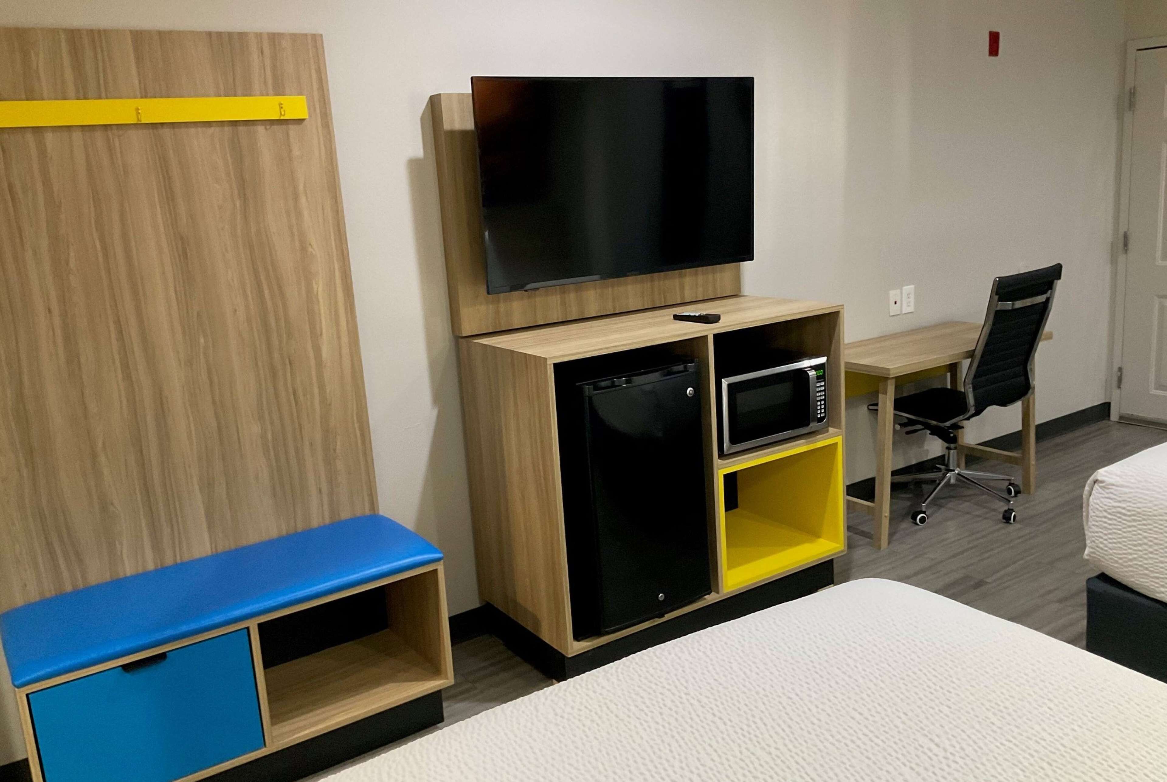 Ein Hotelzimmer mit Bett, Fernseher, kleinem Kühlschrank, Mikrowelle, Schreibtisch und Stuhl.