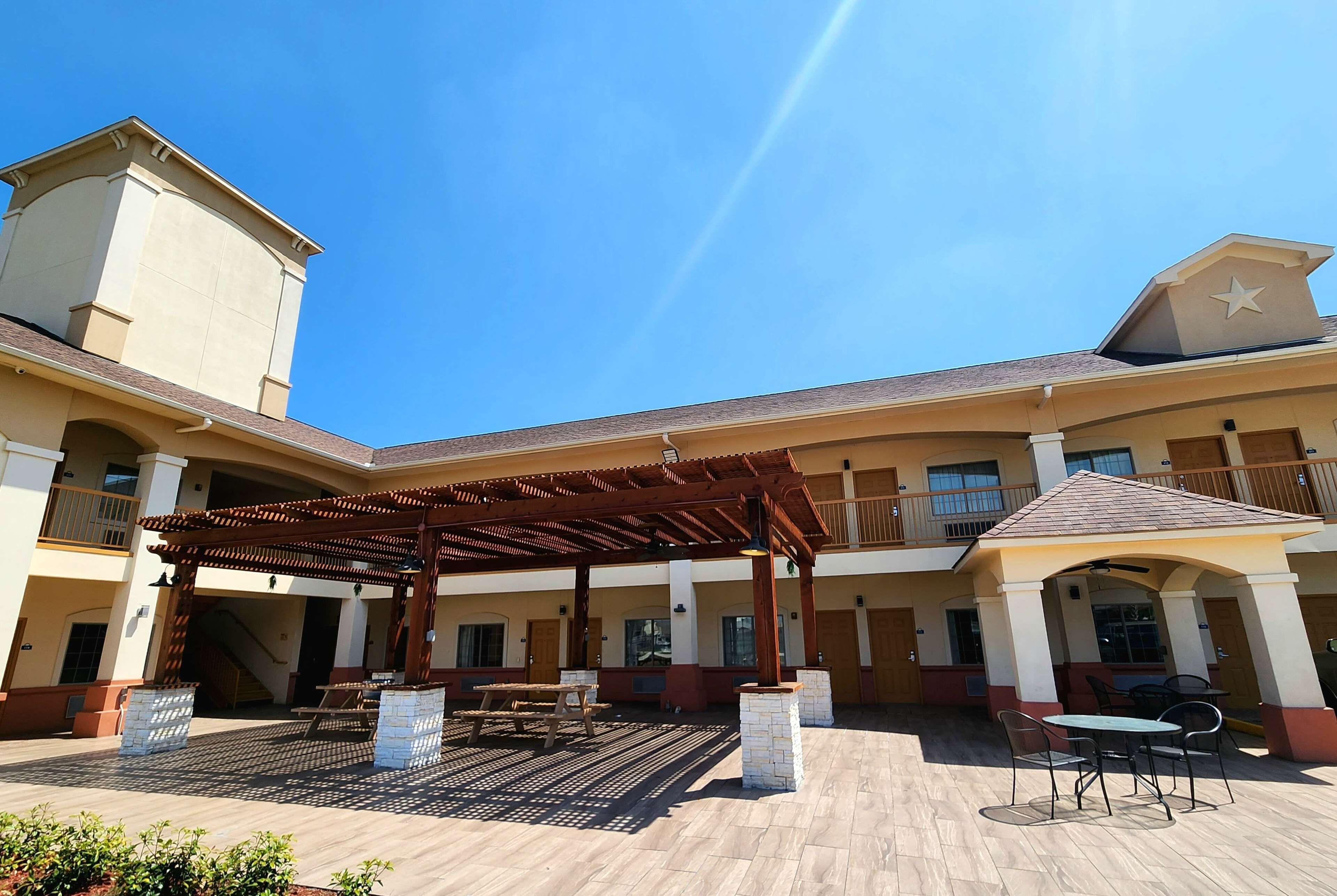 Pátio de hotel com área de estar coberta, mesas ao ar livre e uma fonte central.